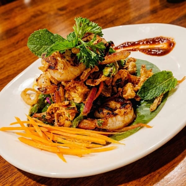 Grilled shrimp salad with crispy toppings, fresh herbs, shredded carrots, and a sauce drizzle.