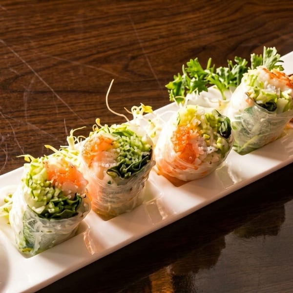Four fresh spring rolls with shrimp, rice noodles, and vegetables on a white rectangular plate.